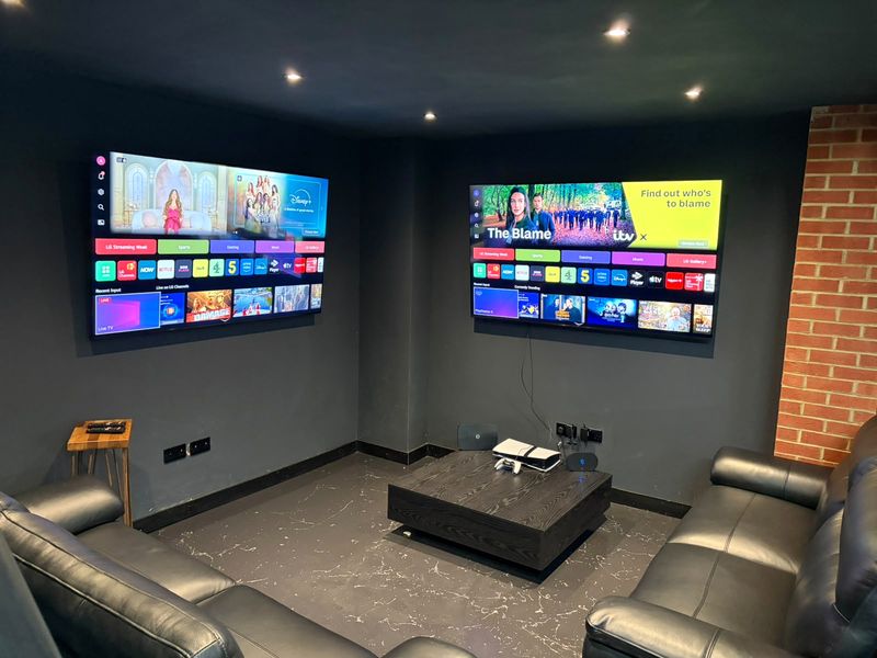 Lounge with black leather sofas, a coffee table and two wall-mounted TVs.