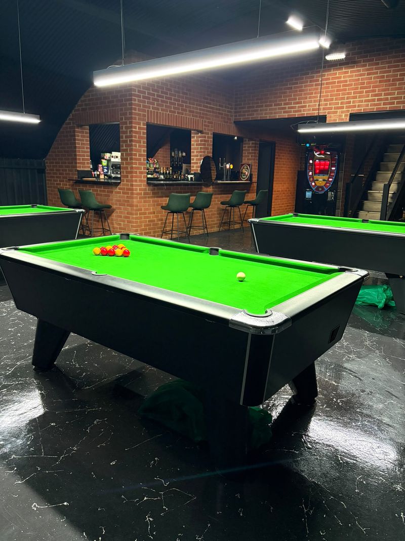 Two green pool tables with the brick-walled bar and stools behind.