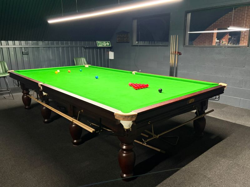 Full snooker table with reds racked, under a long strip light.